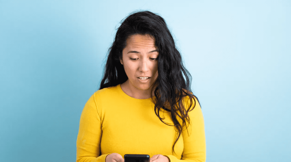 woman with long dark hair looking at her phone in shock