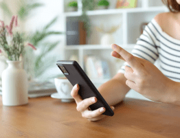 A woman holds a phone she's looking at with one hand and crosses her fingers with the other.