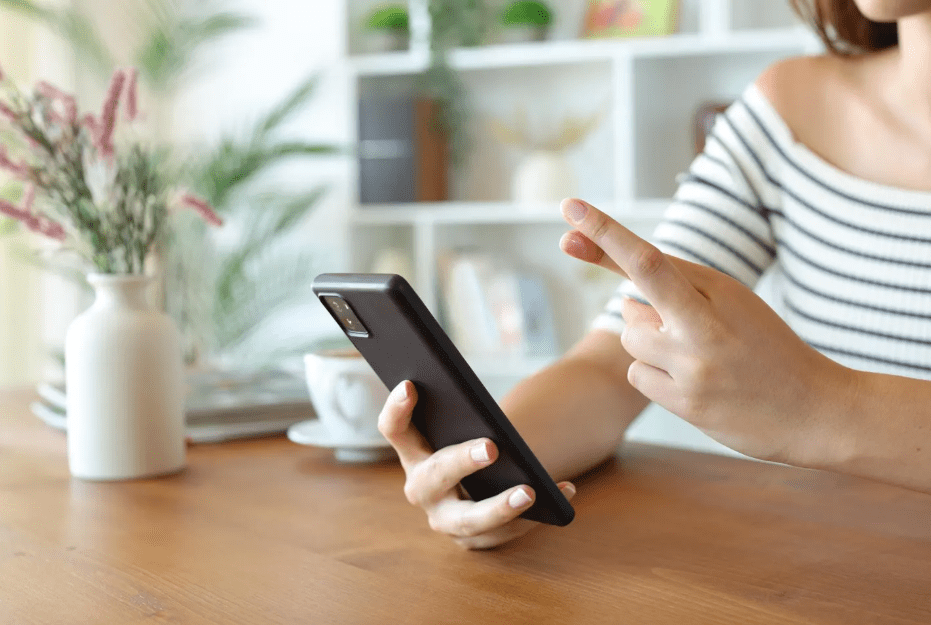 A woman holds a phone she's looking at with one hand and crosses her fingers with the other.
