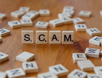 Scrabble tiles scattered on a table top. Four tiles spell "SCAM".