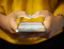 A close up of the hands of a woman wearing a yello as she holds her cell phone