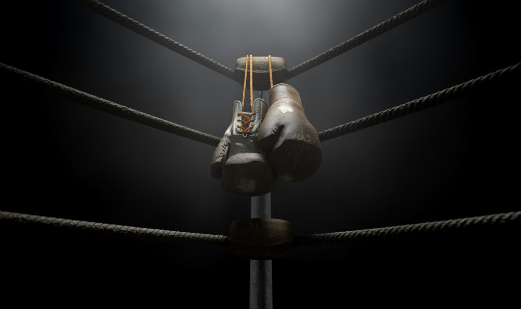 black boxing gloves hanging from the corner of a boxing ring in a dark room