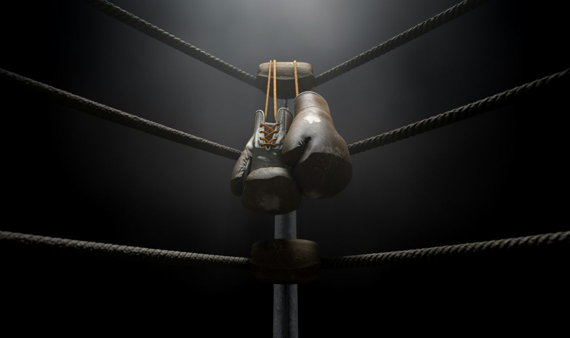 black boxing gloves hanging from the corner of a boxing ring in a dark room