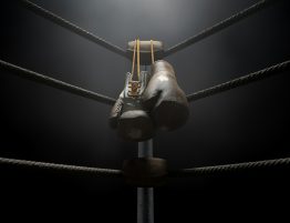 black boxing gloves hanging from the corner of a boxing ring in a dark room