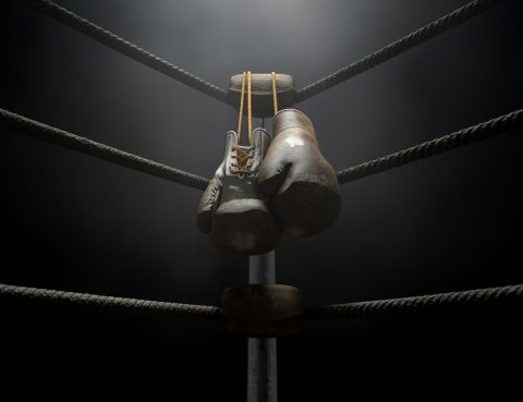 black boxing gloves hanging from the corner of a boxing ring in a dark room