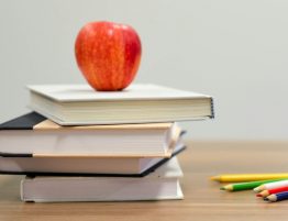 a stack of books with a red apple on the top beside a few colored pencils