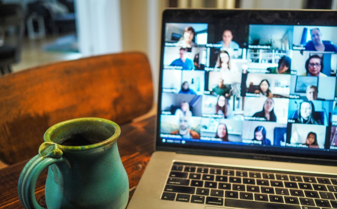 image of a laptop on a table with a video call meeting on its screen next to a blue mug