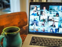 image of a laptop on a table with a video call meeting on its screen next to a blue mug