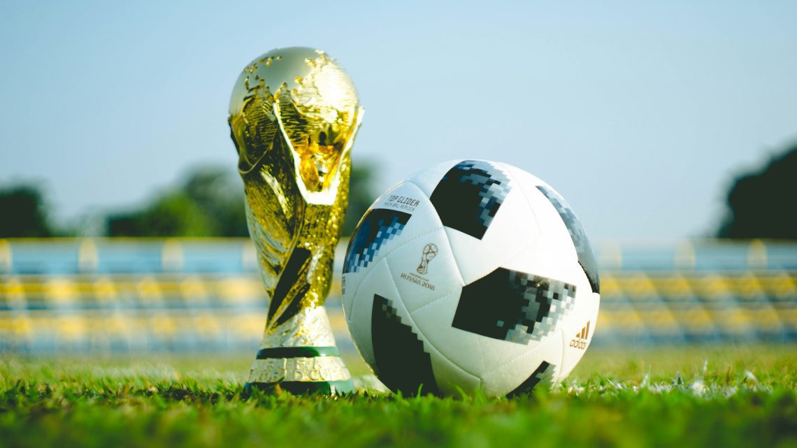 a close up of the FIFA trophy and a soccer ball on a grassy field
