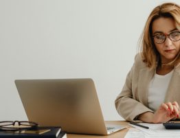 woman using a calculator at her desk which has a laptop and paperwork on it