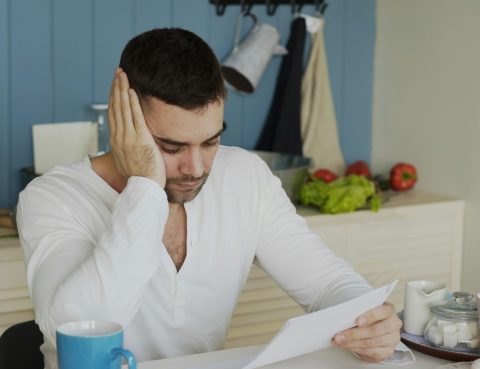 A man at a breakfast table looks at a letter with worry on his face
