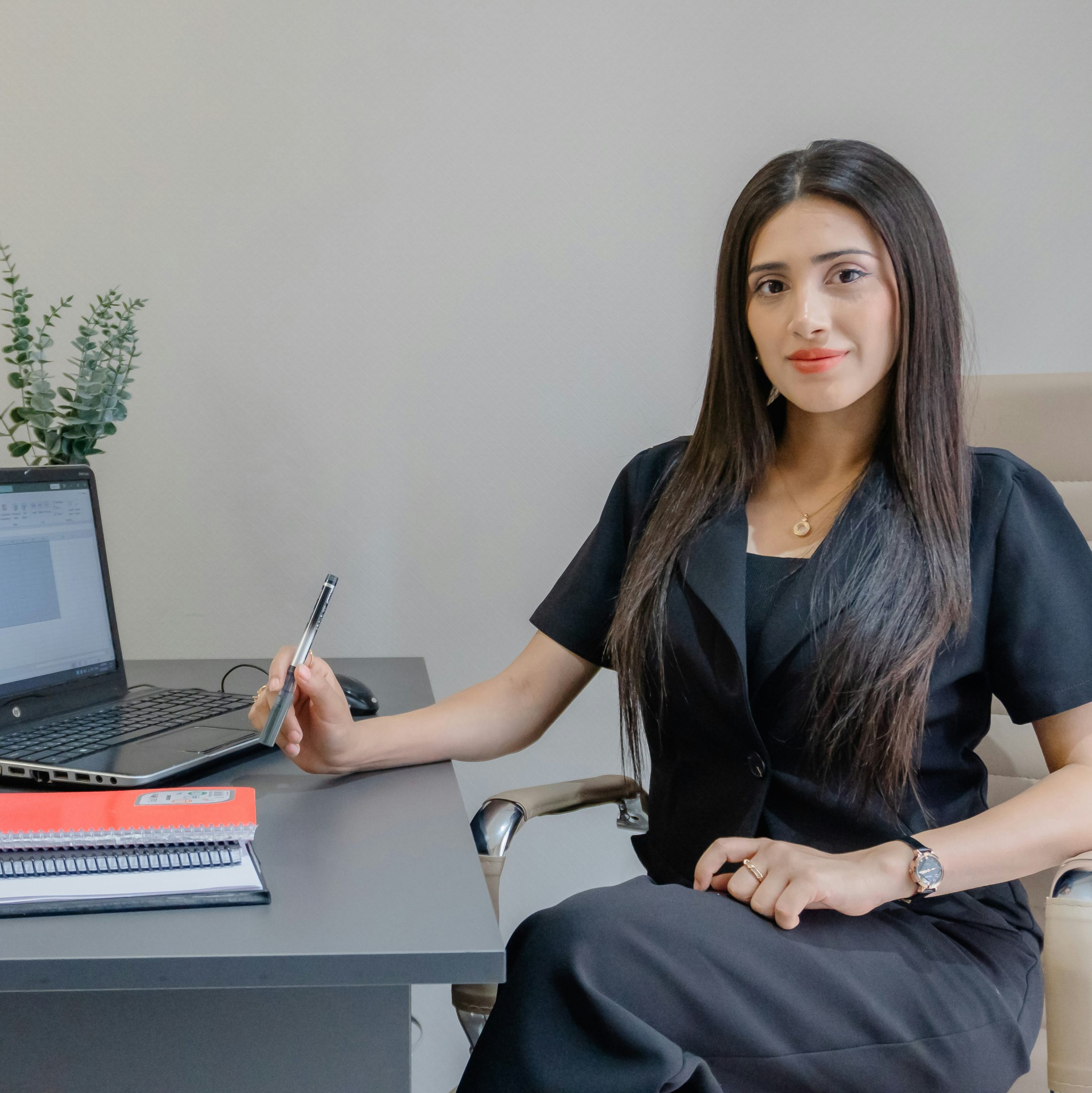 Woman with a pen in her hand, sitting at her desk and looking at the camera