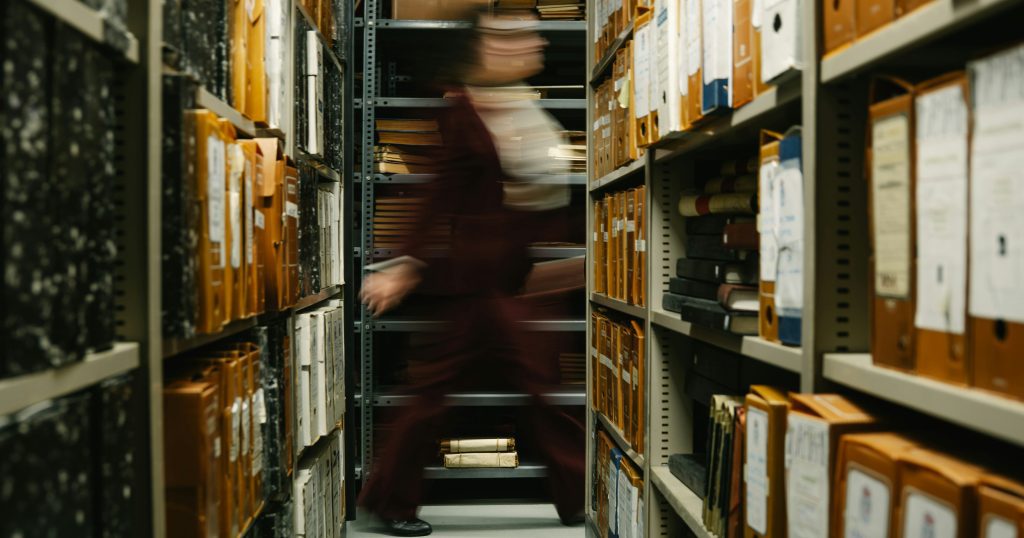 photo of blurred woman walking past shelves full of files