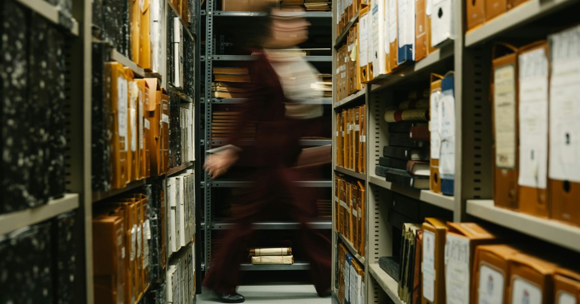 photo of blurred woman walking past shelves full of files