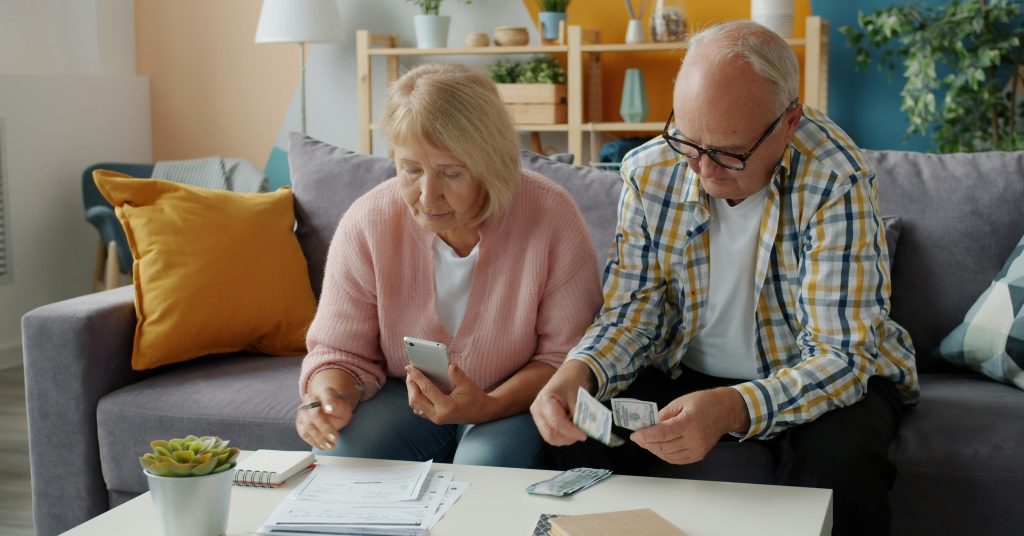 a couple sitting on the couch looking at paperwork and counting money
