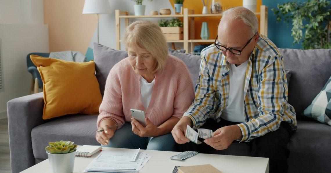 a couple sitting on the couch looking at paperwork and counting money