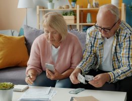 a couple sitting on the couch looking at paperwork and counting money